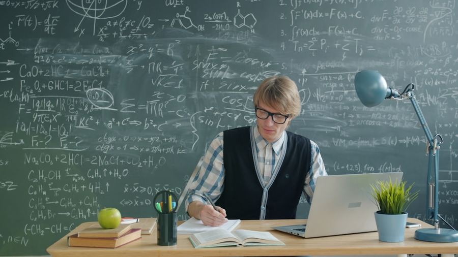 A student studying at a desk in front of a chalkboard